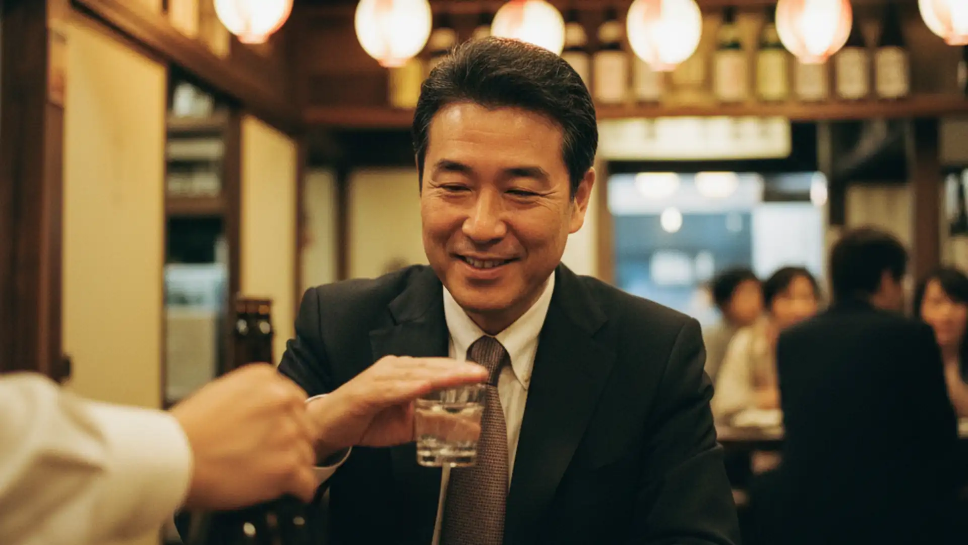 Businessman politely covering his glass to decline a refill at a Japanese izakaya