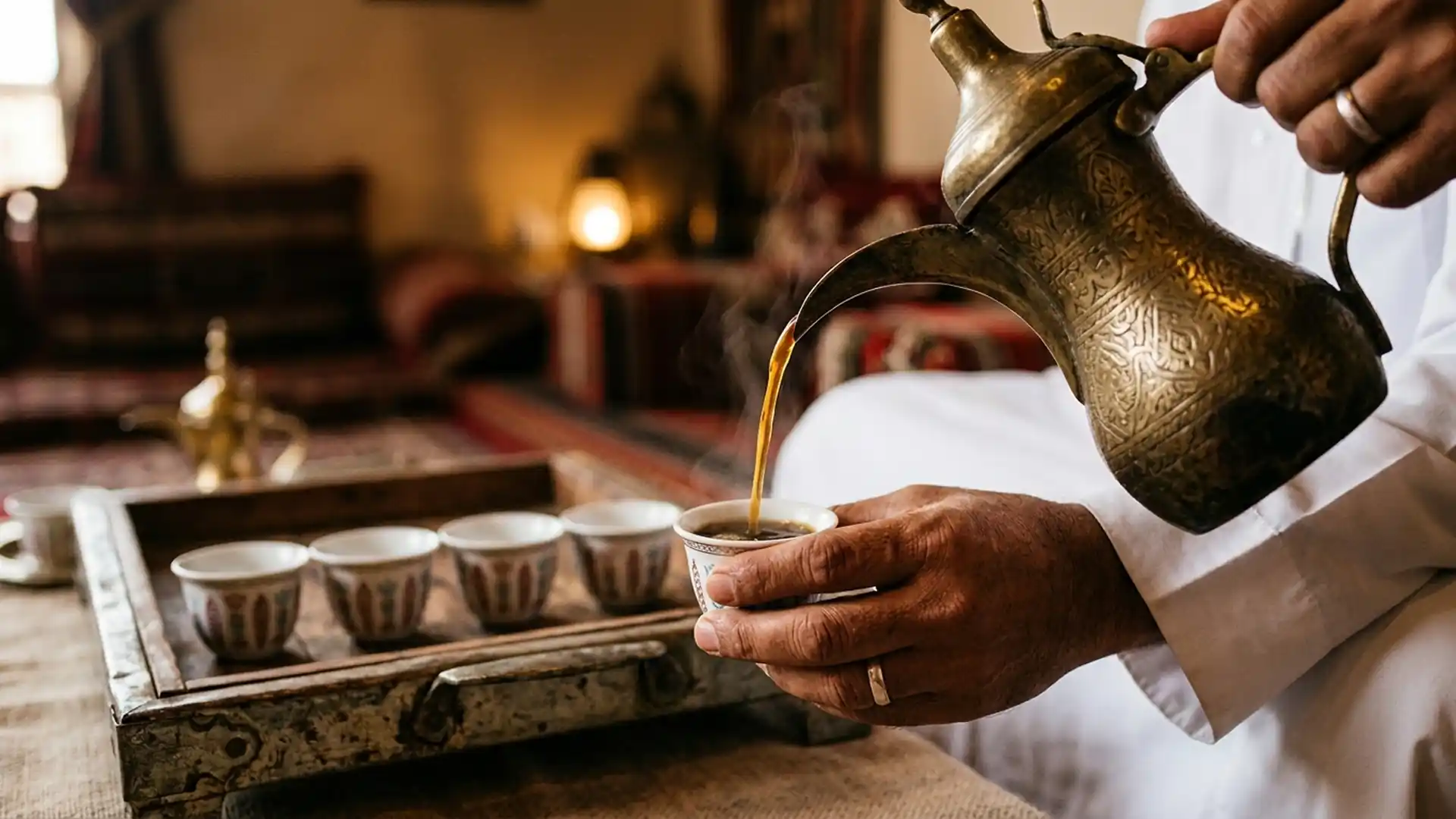 Brass dallah pouring Arabic gahwa coffee into a small finjan cup held in the right hand